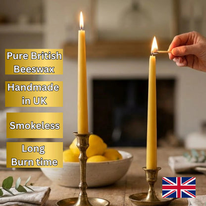 Two tall yellow beeswax taper candles in brass holders on a table, with one candle lit and a hand holding a match beside it. Text on the left reads 'Pure British Beeswax', 'Handmade in UK', 'Smokeless', and 'Long Burn time', with a small UK flag at the bottom right.
