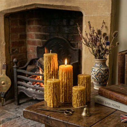 Four textured beeswax pillars arranged on a rustic oak table next to a traditional British stone fireplace, creating a cozy, Victorian-inspired atmosphere perfect for home decor.