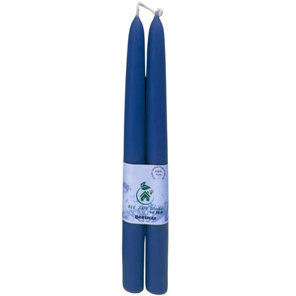 Two blue taper candles wrapped together with a white paper band featuring a green logo and text, set against a plain white background.