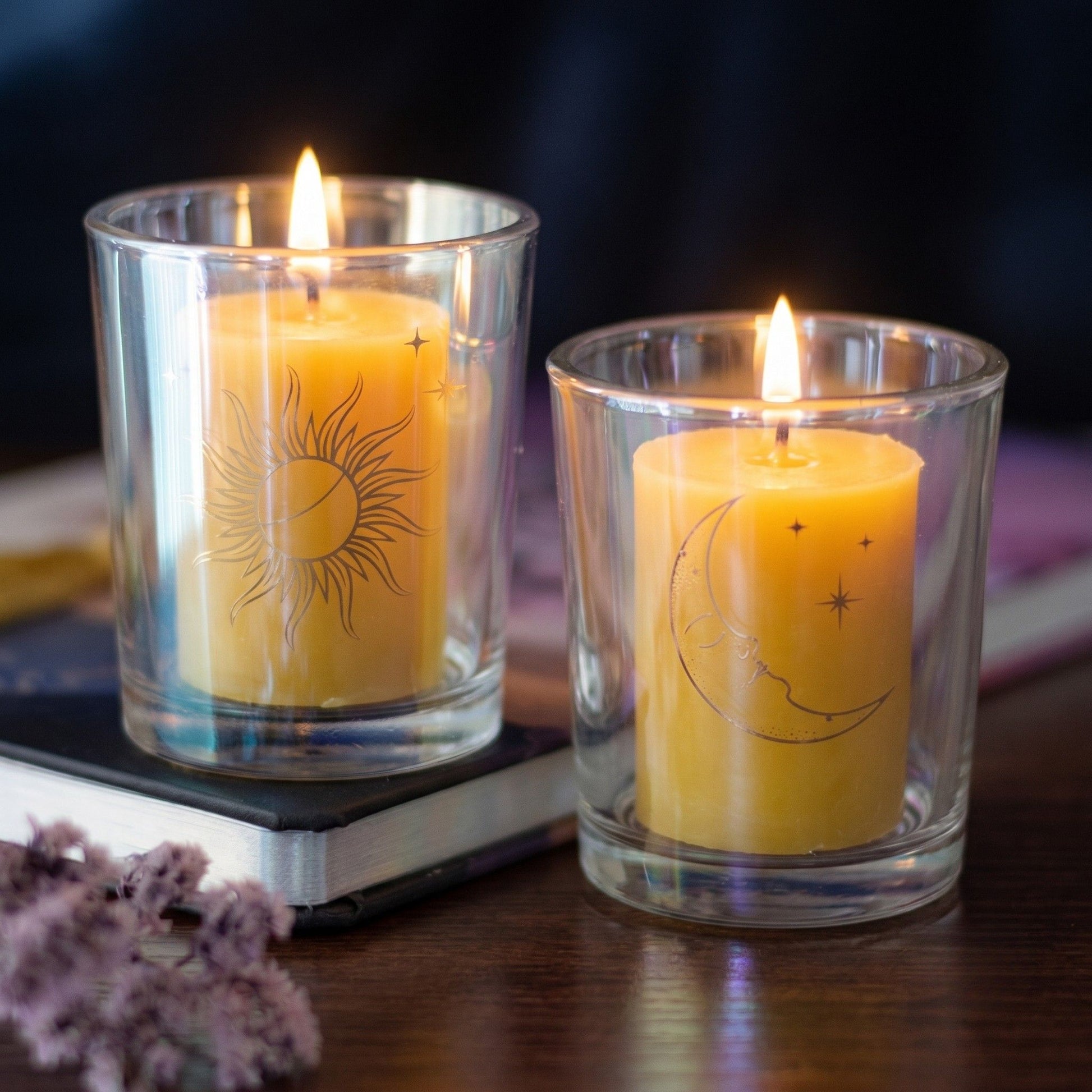 Two lit candles in glass holders with celestial designs on a dark background