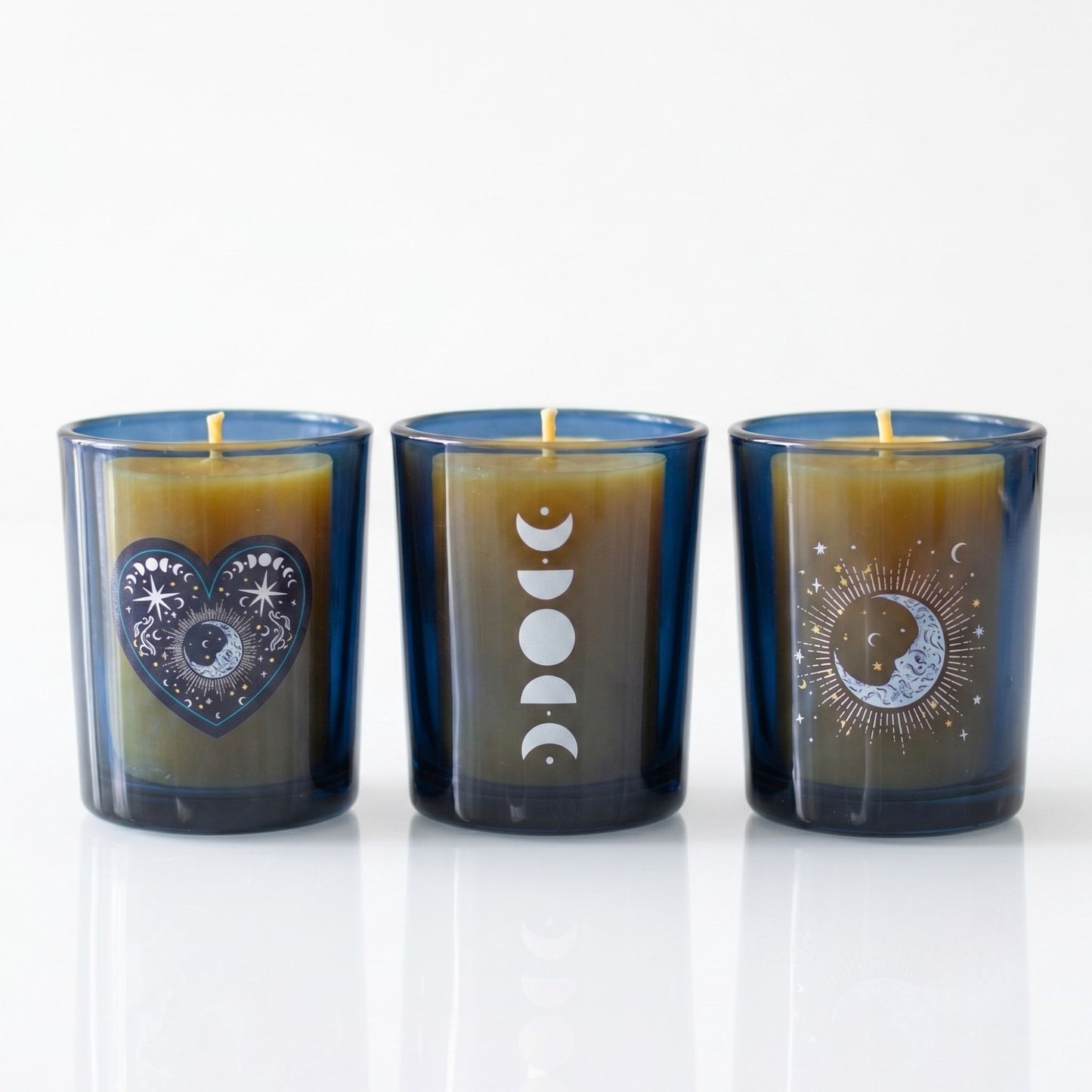 Trio of dark blue glass celestial tealight holders featuring silver moon phases and a mystical heart emblem on a white background.