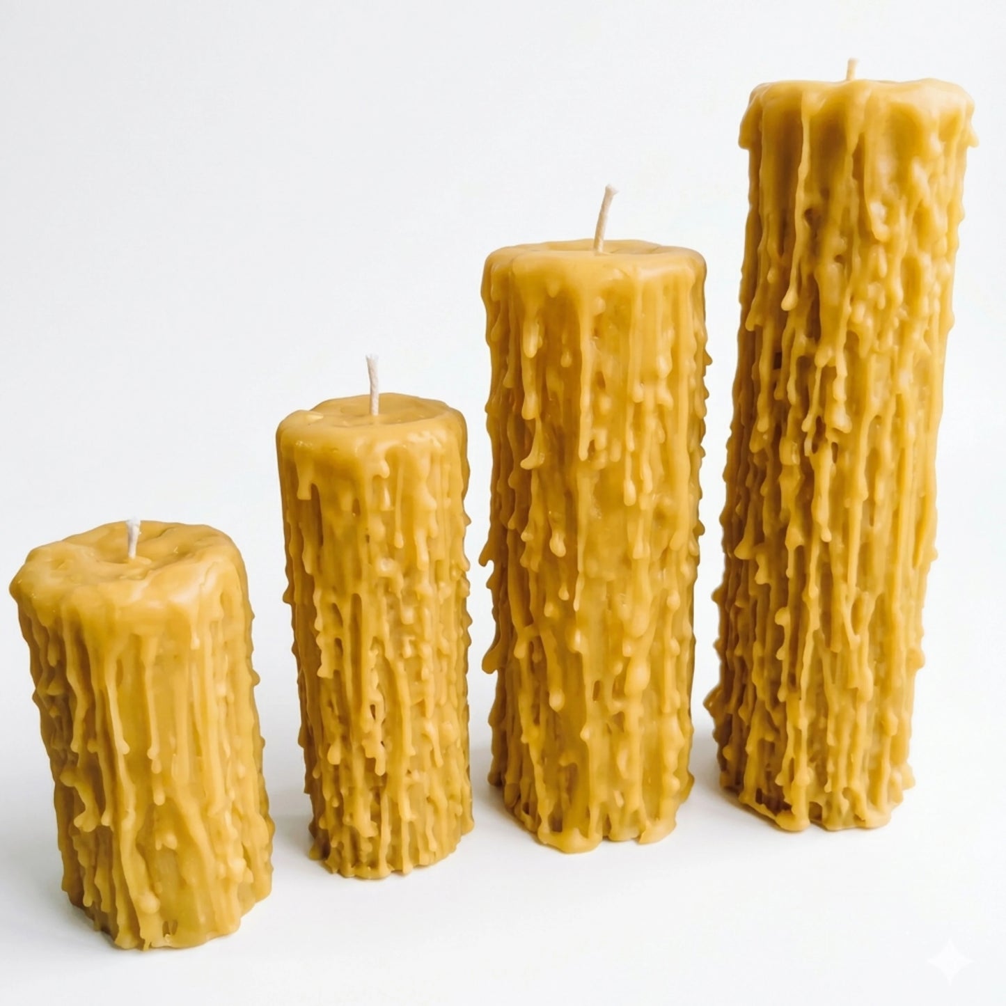 A professional product shot of four hand-dripped beeswax pillar candles in varying heights, ranging from 100mm to 250mm, arranged in a diagonal line on a clean white background.